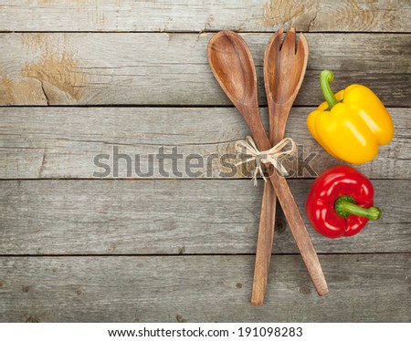 Colorful bell peppers and kitchen utensils over wooden table background with copy space