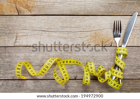 Measure tape with knife and fork. Diet food on wooden table with copy space