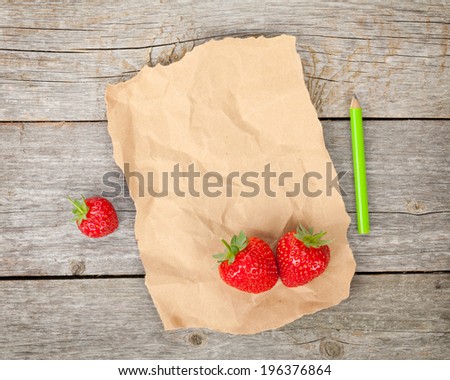 Blank paper with copy space and ripe strawberries over wooden table backgroun