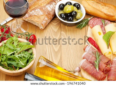 Red wine with cheese, prosciutto, bread, vegetables and spices on wooden table with copy space