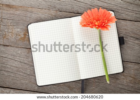 Blank notepad and orange gerbera flower on wooden table background