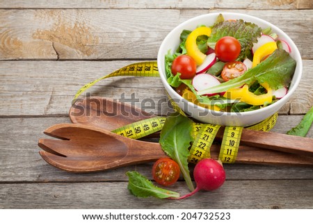 Fresh healthy salad, utensil and measure tape on wooden table background