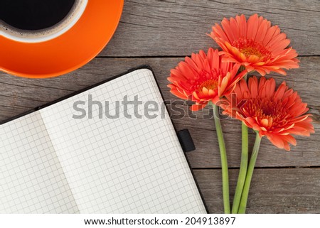 Blank notepad, coffee cup and orange gerbera flowers on wooden table background