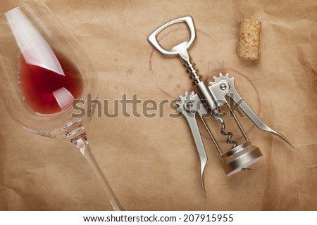 Wine glass, cork and corkscrew with red wine stains on brown paper background