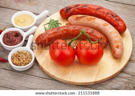 Various grilled sausages with condiments and tomatoes on cutting board