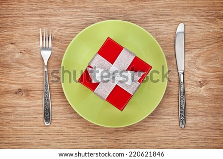 Gift box on plate and silverware over wooden table background