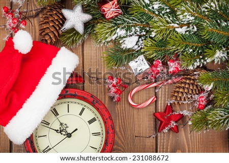 Christmas wooden background with snow fir tree, decor and clock with santa hat. View from above