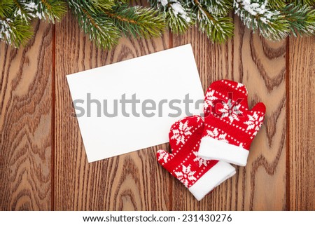 Christmas greeting card or photo frame and mittens over wooden table with snow fir tree. View from above