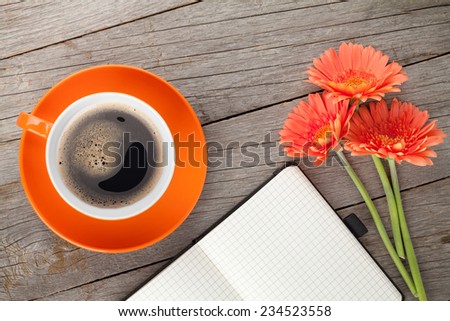 Blank notepad, coffee cup and orange gerbera flowers on wooden table background