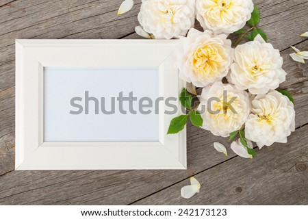 Blank photo frame and white roses over wooden table background