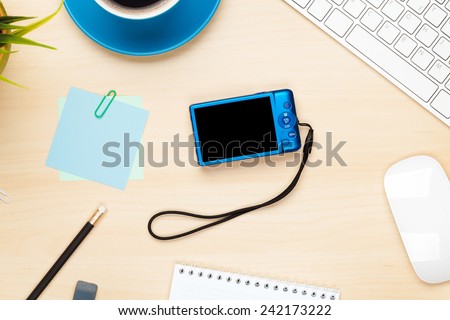 Photo camera on office table with notepad, computer and coffee cup. View from above