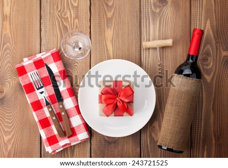 Table setting with gift box on plate, wine glass and red wine bottle. View from above over rustic wooden table background