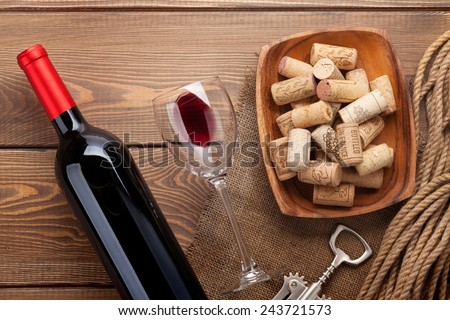 Red wine bottle, glass of wine, bowl with corks and corkscrew. View from above over rustic wooden table background