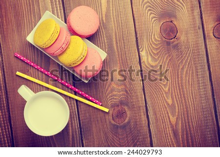 Colorful macaron cookies and cup of milk on wooden table background with copy space. Toned