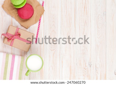 Colorful macarons, cup of milk and gift box on white wooden table with copy space