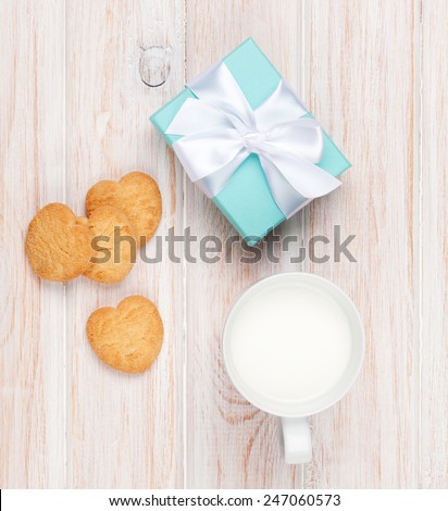 Cup of milk, heart shaped cookies and gift box on white wooden table