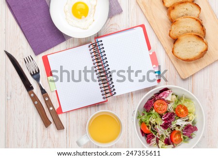 Healthy breakfast with fried egg, toasts and salad on white wooden table with notepad for copy space