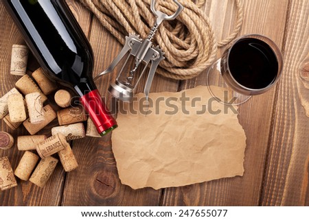 Red wine, corks, corkscrew and piece of paper for copy space on wooden table background