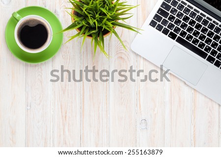 Office desk table with laptop computer, coffee cup and flower. Top view with copy space