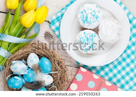 Easter background with blue and white eggs in nest, yellow tulips and traditional cakes. Top view