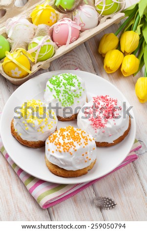 Easter with yellow tulips, colorful eggs and traditional cakes over white wooden table. Top view