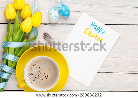 Easter greeting card with blue and white eggs, yellow tulips and coffee cup over white wood. Top view with copy space