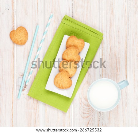 Cup of milk and heart shaped cookies on white wooden table