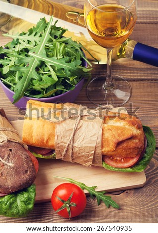 Two sandwiches and white wine glass on wooden table. Toned