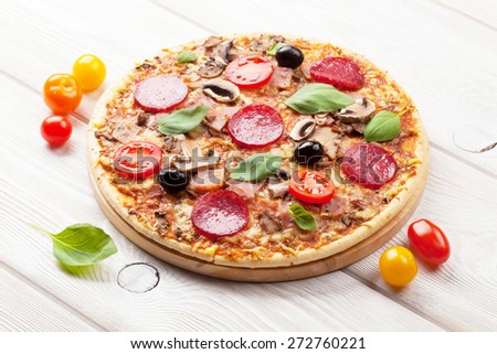 Italian pizza with pepperoni, tomatoes, olives and basil on wooden table