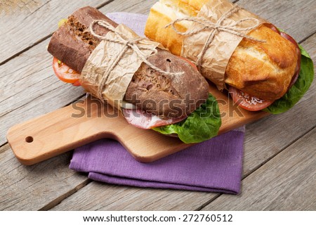 Two sandwiches with salad, ham, cheese and tomatoes on cutting board