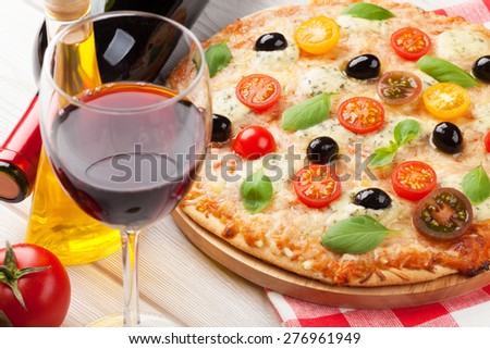Italian pizza with cheese, tomatoes, olives, basil and red wine on wooden table