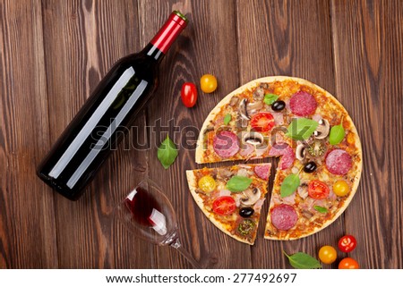 Italian pizza with pepperoni, tomatoes, olives, basil and red wine on wooden table. Top view