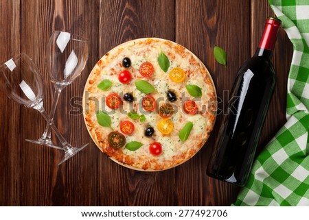 Italian pizza with cheese, tomatoes, olives, basil and red wine on wooden table. Top view
