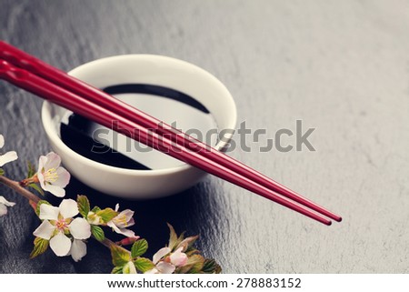 Japanese sushi chopsticks, soy sauce bowl and sakura blossom on black stone background. Top view with copy space. Toned