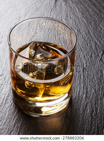 Glass of scotch whiskey with ice on black stone table