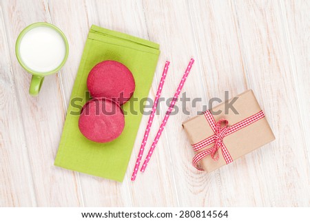 Colorful macarons, cup of milk and gift box on white wooden table