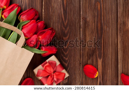 Red tulips bouquet in paper bag and gift box over wooden table background with copy space
