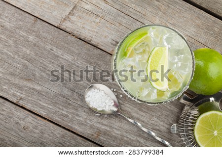 Classic margarita cocktail with salty rim on wooden table with limes and drink utensils