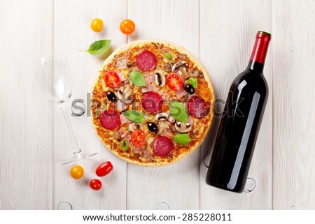 Italian pizza with pepperoni, tomatoes, olives, basil and red wine on wooden table. Top view