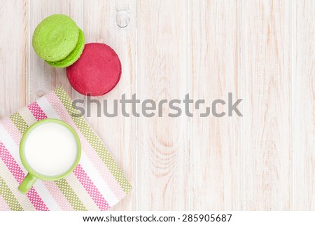 Colorful macarons and cup of milk on white wooden table with copy space