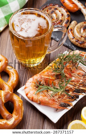 Beer mug, grilled shrimps, sausages and pretzel on wooden table