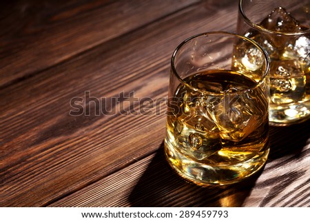 Glasses of whiskey with ice on wooden table with copy space
