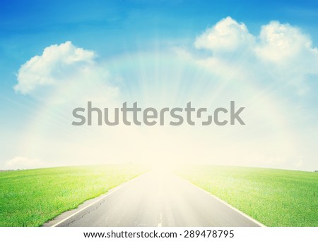 Summer landscape with endless asphalt road through the green field and blue sky with rainbow