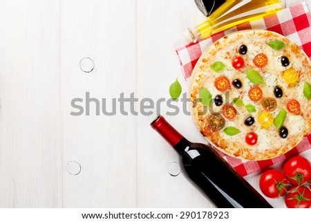 Italian pizza with cheese, tomatoes, olives, basil and red wine on wooden table. Top view with copy space