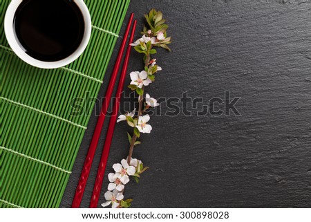 Japanese sushi chopsticks, soy sauce bowl and sakura blossom on black stone background. Top view with copy space