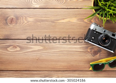 Camera, sunglasses and flower on office wooden desk table. Top view with copy space
