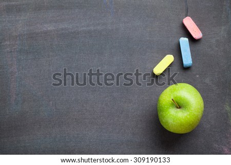Colorful chalk and apple on blackboard background. Top view with copy space