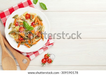 Colorful penne pasta with tomatoes and basil on wooden table. Top view with copy space