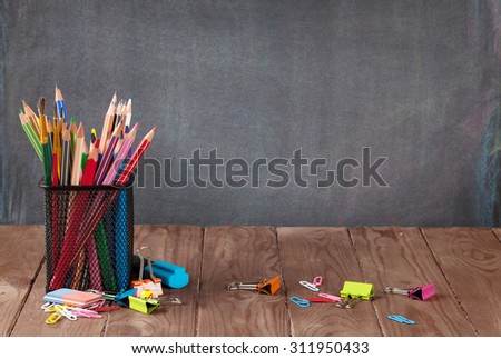 School and office supplies on classroom table in front of blackboard. View with copy space