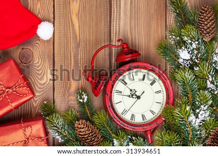 Christmas wooden background with clock, snow fir tree, gift boxes and santa hat
